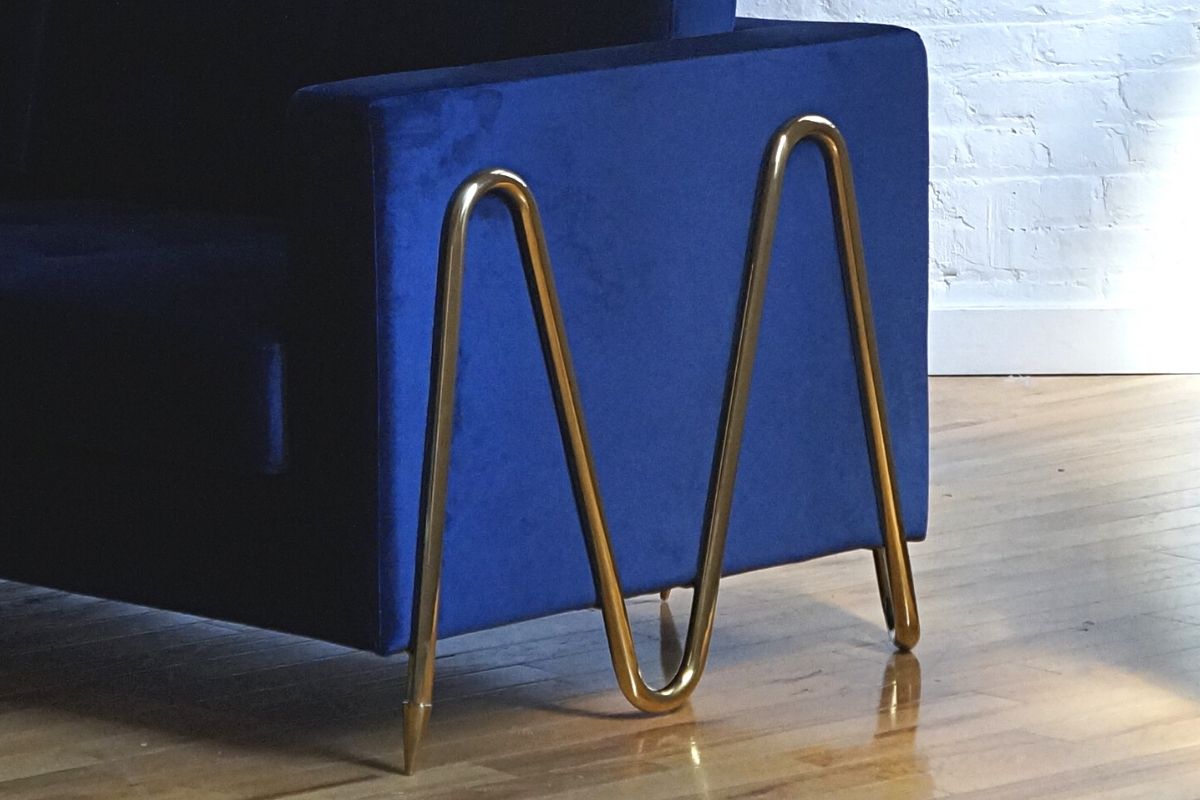 Invention blue couch zoomed in angled view of gold zig zag patterned feet, blue velvet couch, royal blue couch, gold velvet, biscuit tufted couch, modern couch, mid-century modern couch, gold legs, blue and gold couch