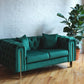 Song emerald green velvet loveseat with gold legs angled view alongside plant, green velvet setee, tufted sweetheart couch, modern loveseat, chesterfield couch, mid-century modern couch product image