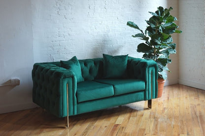Song emerald green velvet loveseat with gold legs angled view alongside plant, green velvet setee, tufted sweetheart couch, modern loveseat, chesterfield couch, mid-century modern couch product image